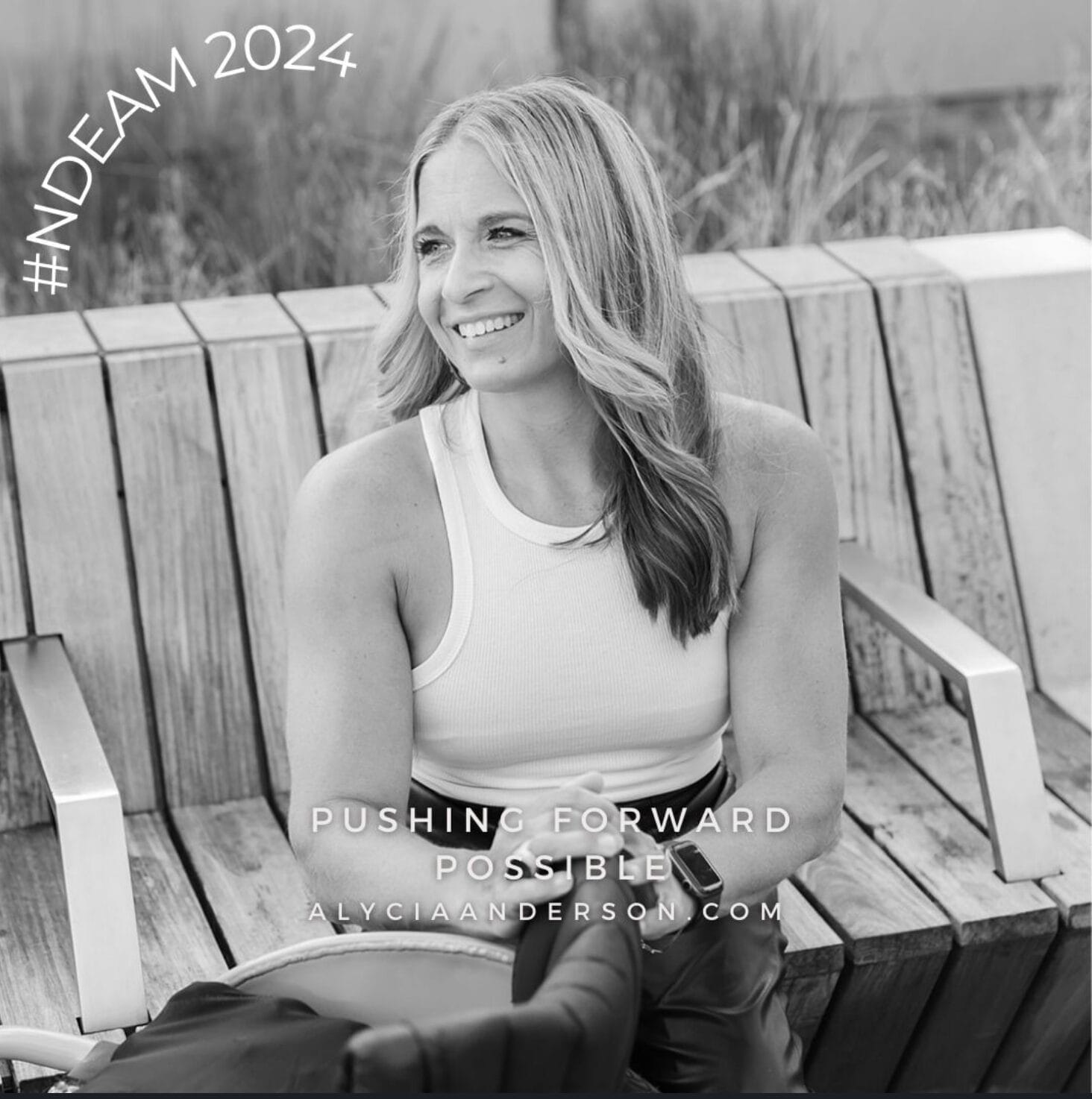 Alycia sitting on a bench with hands resting on her wheelchair looking to the left smiling